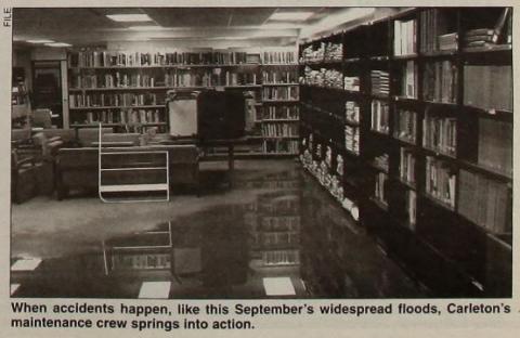 A photograph of flood waters in a room with books, bookshelves, chairs and tables, which have been moved away from the water.