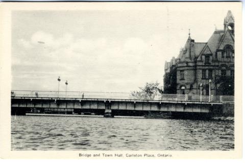 Rectangular postcard with black and white photograph of "Bridge and Town Hall, Carleton Place, Ontario". Shows bridge over Mississippi River and portion of Town Hall to right. Three people walking over bridge. Stone building visible in background behind bridge to left. Unused. Printed on reverse: "The Photoflatine Engraving Co. Ltd., Toronto".